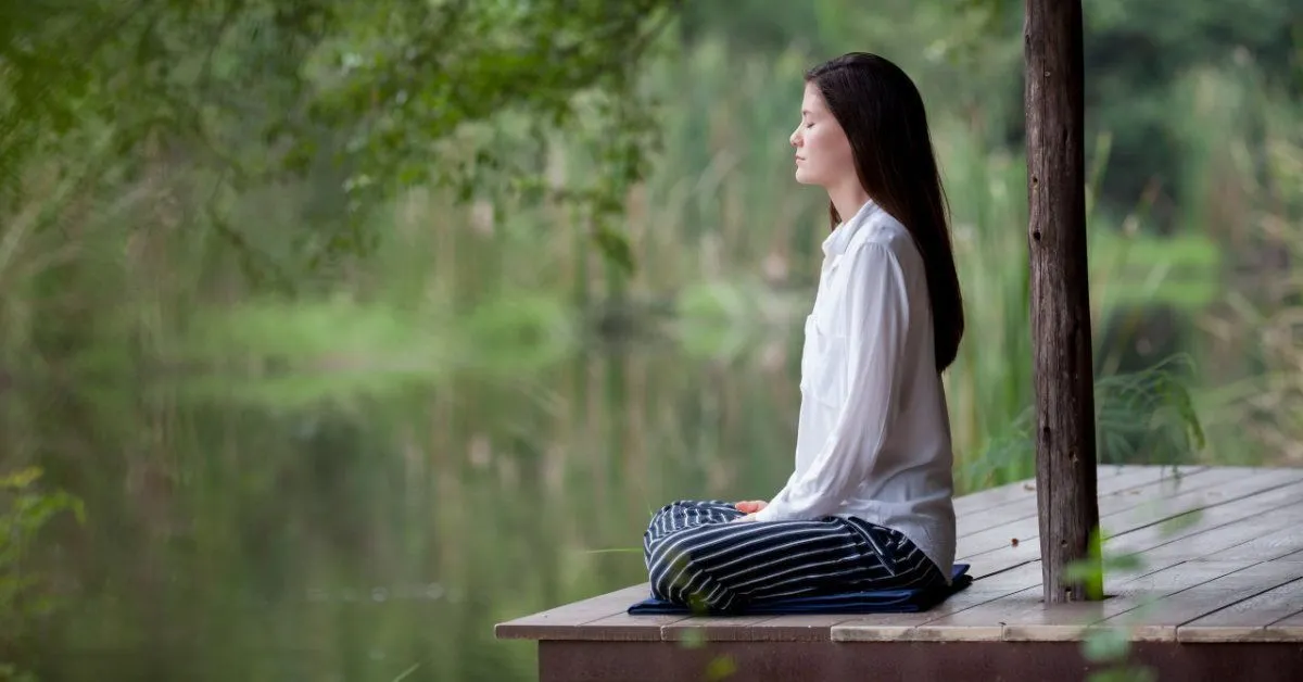 Fotografía de una mujer meditando junto a un lago o estanque