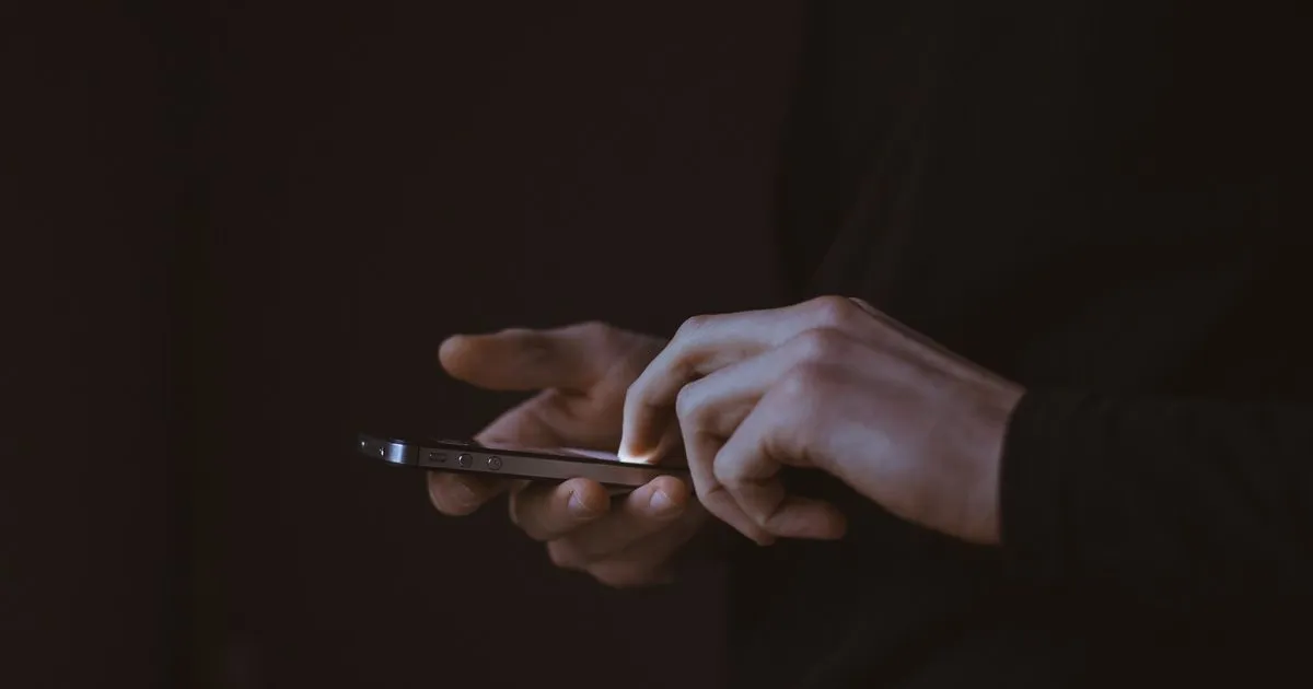 Fotografía de unas manos sujetando un teléfono móvil en un fondo oscuro