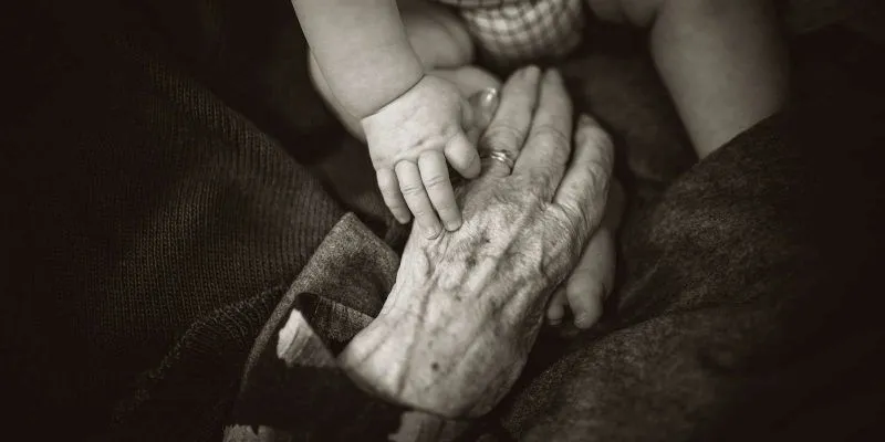 Fotografía de la mano de una anciana tocando la mano y el pie de un bebé. Rod Long (Unsplash).